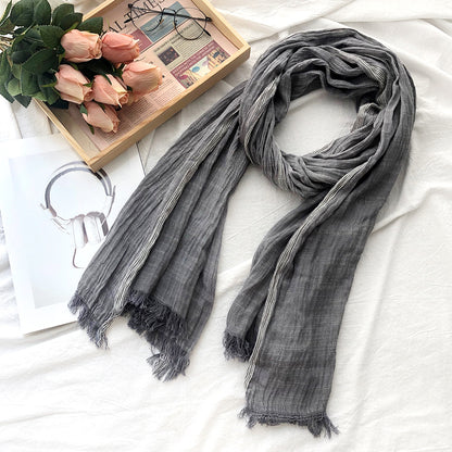 Gray scarf with tassels on a white surface with a wooden tray of pink roses and glasses.