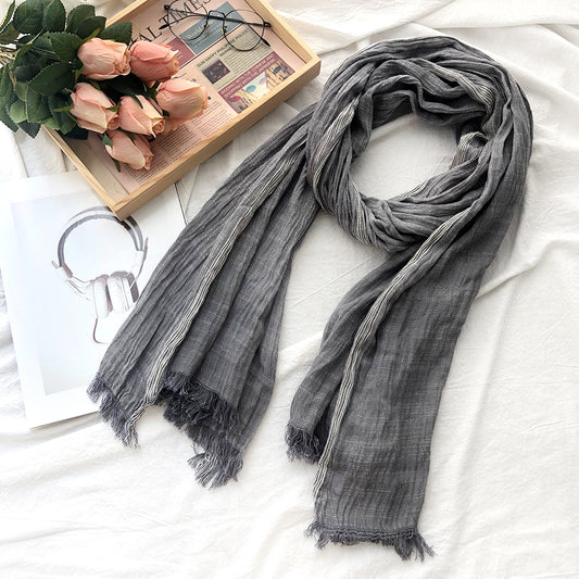 Gray scarf with tassels on a white surface with a wooden tray of pink roses and glasses.