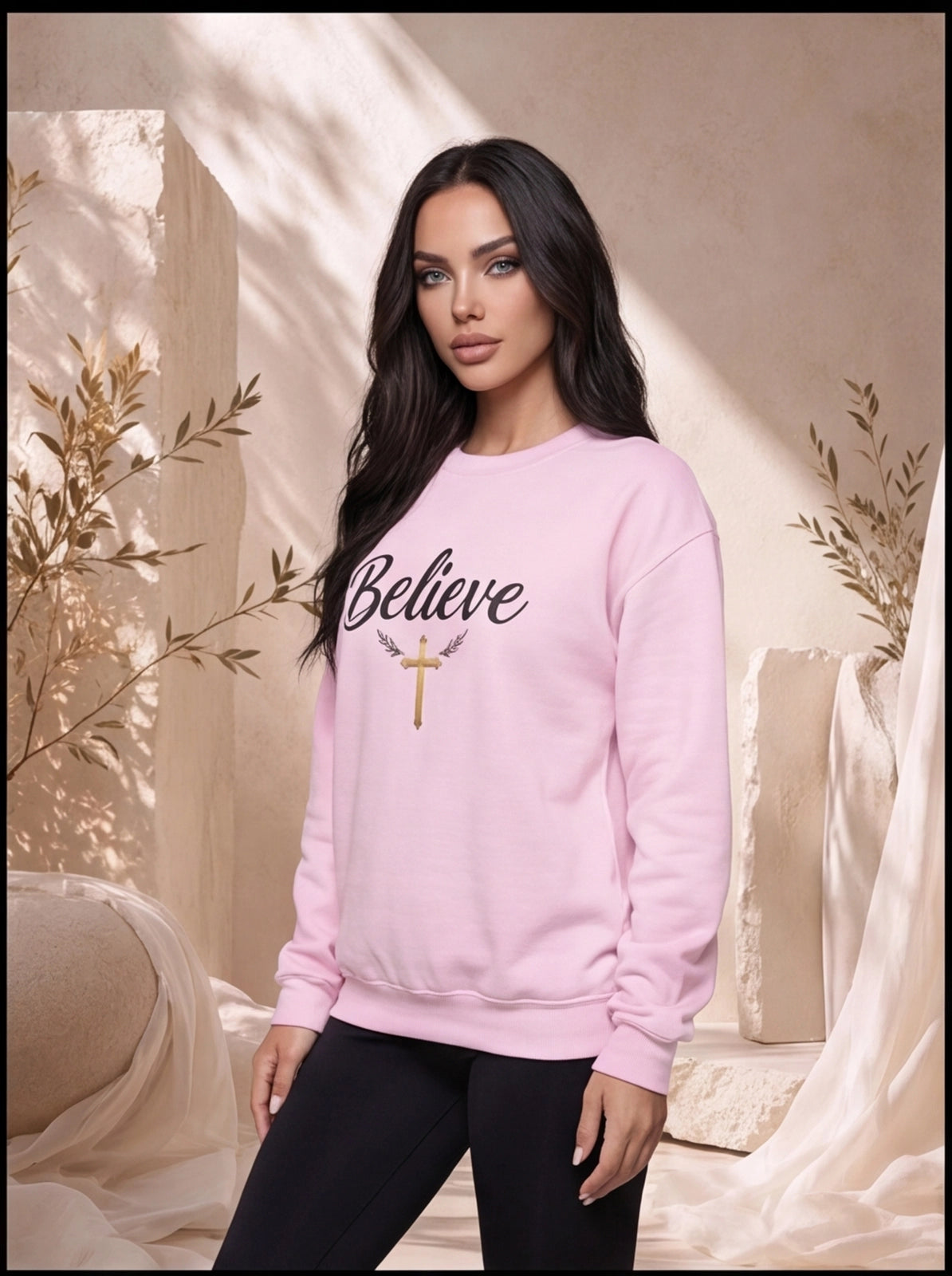 Woman wearing a pink sweatshirt with 'Believe' and a cross design, standing in a softly lit room.