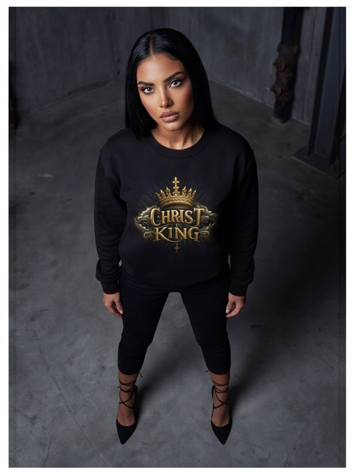 Woman wearing a black sweatshirt with 'Christ King' text and crown graphic on a dark background