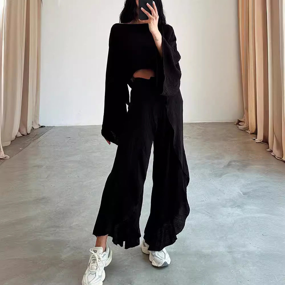 Person wearing a black outfit with wide-leg pants in a minimalistic room.