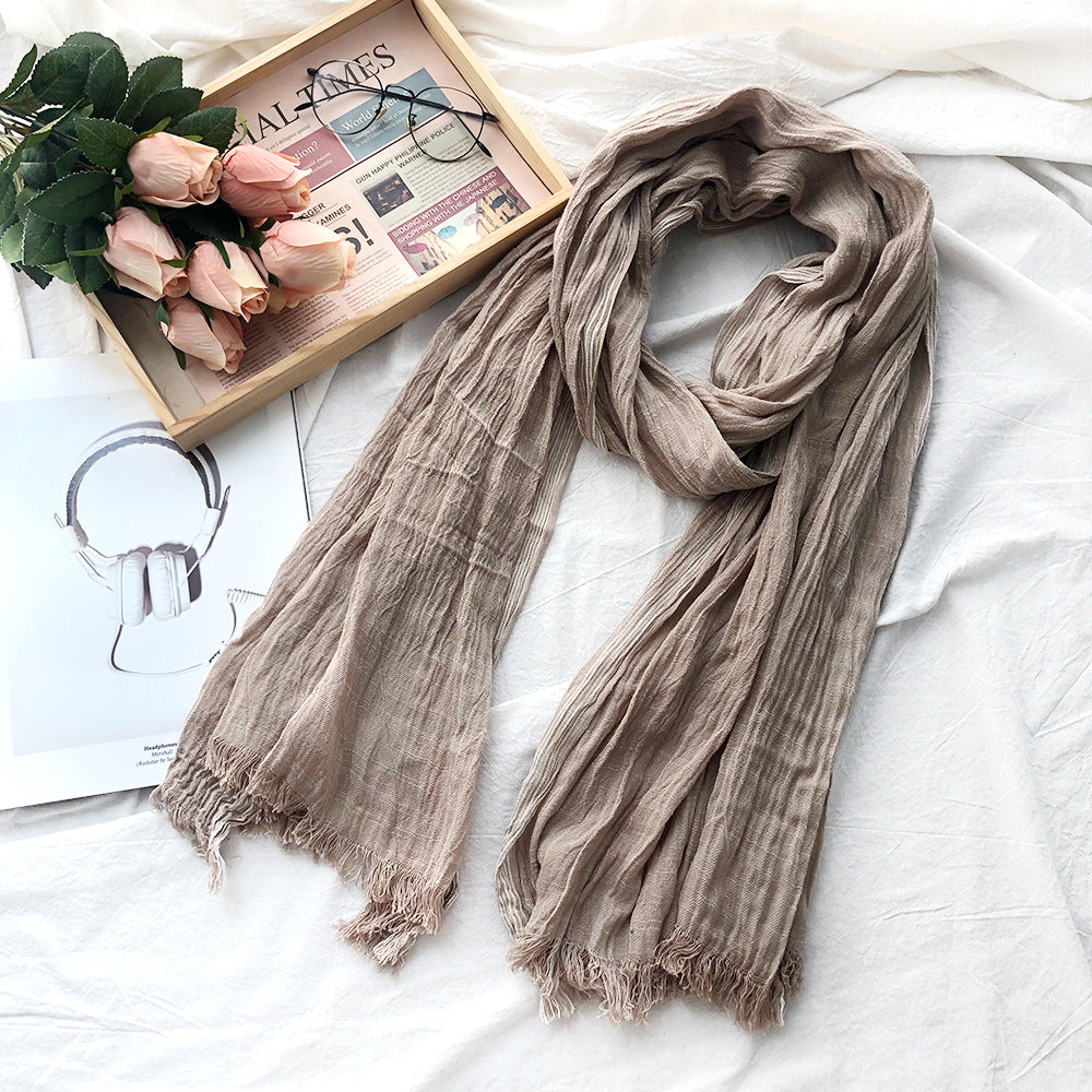 Beige scarf on a white surface with flowers and a newspaper in the background