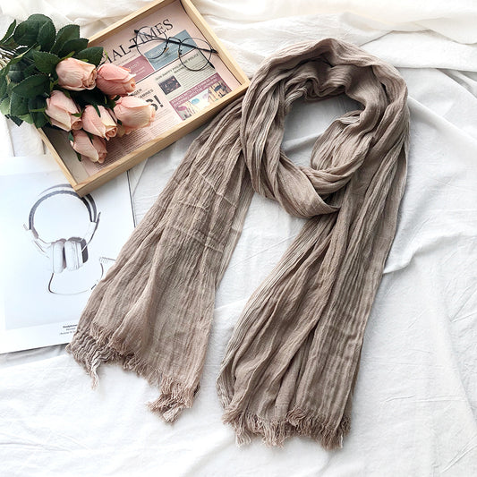 Beige scarf on a white surface with flowers and a newspaper in the background