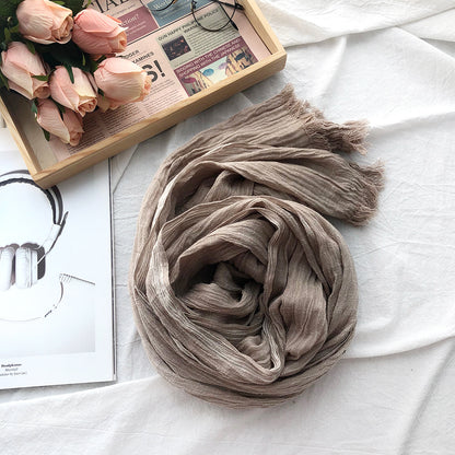Brown scarf on a white surface with flowers and a magazine in the background