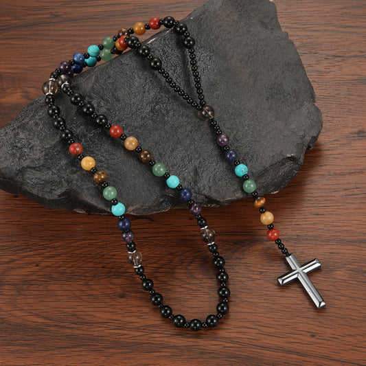 Multicolored beaded necklace with a silver cross pendant on a dark stone surface.