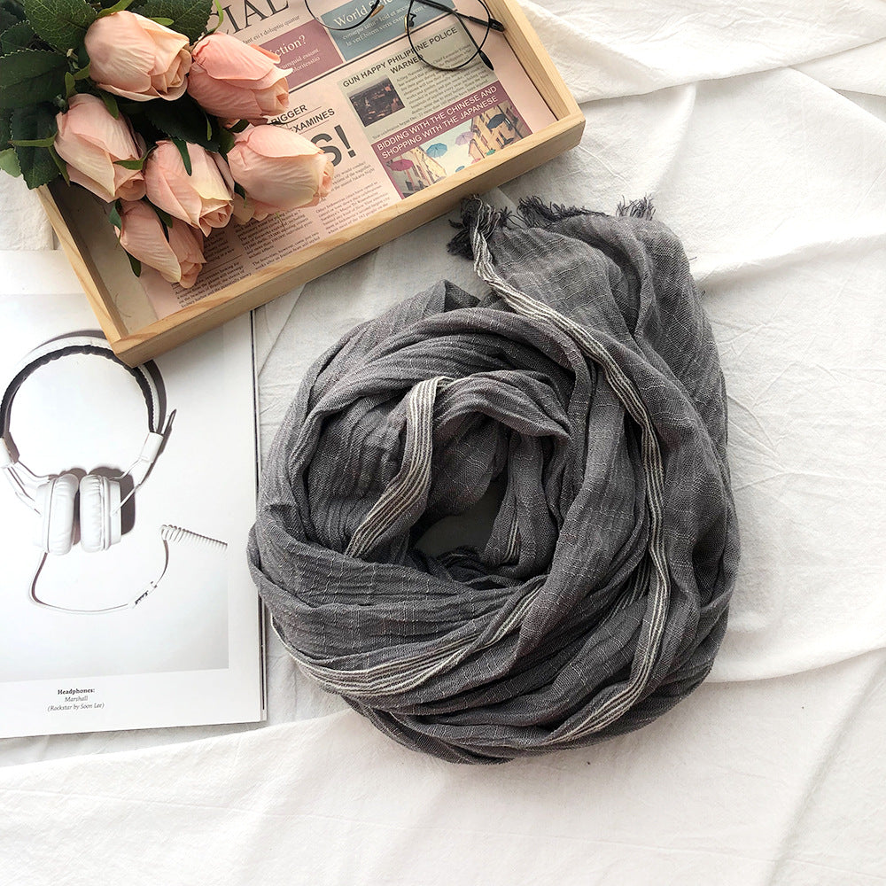 Gray scarf on a white surface with a wooden tray holding pink roses and a magazine.