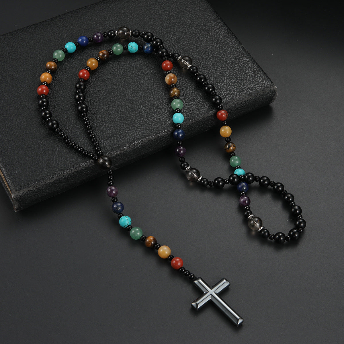 Multicolored beaded necklace with a silver cross pendant on a dark surface